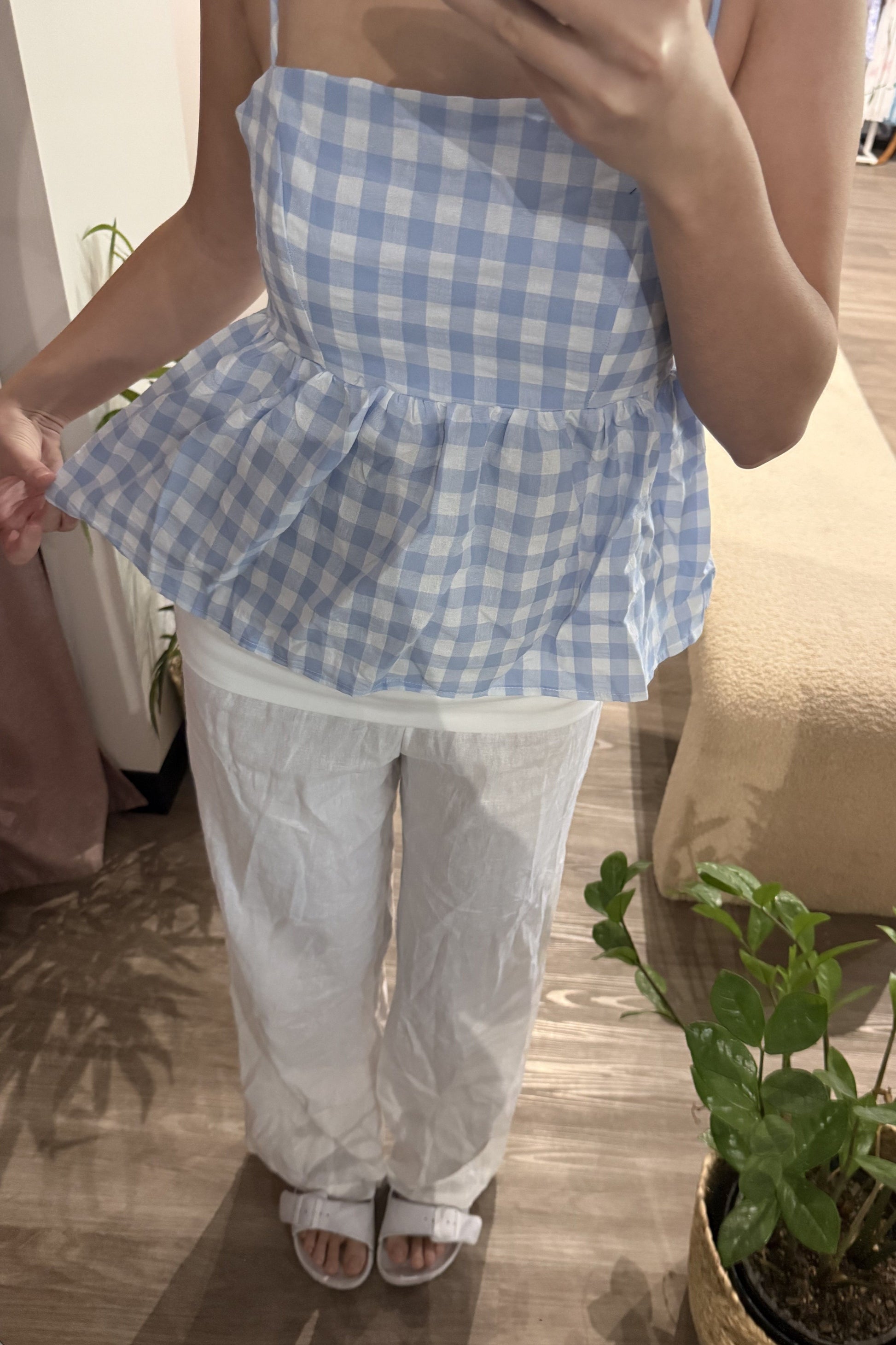 Person wearing a blue and white checkered top and white pants indoors.